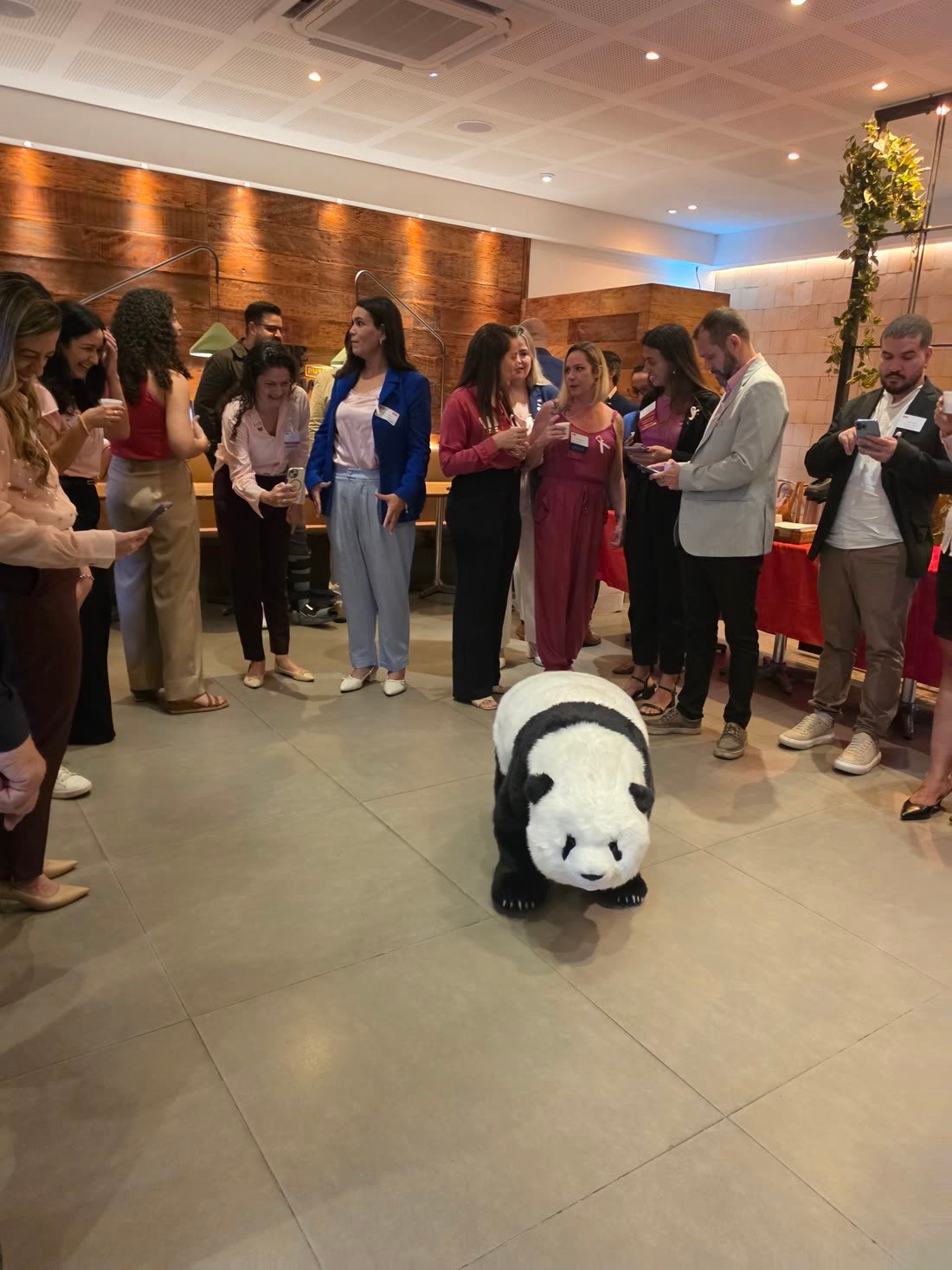 Panda robô caminhando no meio de uma roda de convidados, com várias pessoas filmando com o celular