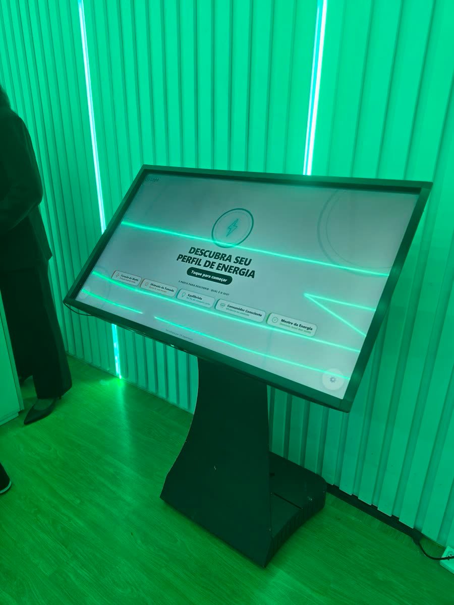 Totem de chão com tela de 43 polegadas inclinada, em estande iluminado por neon verde, aberto na tela inicial do game de perfil
