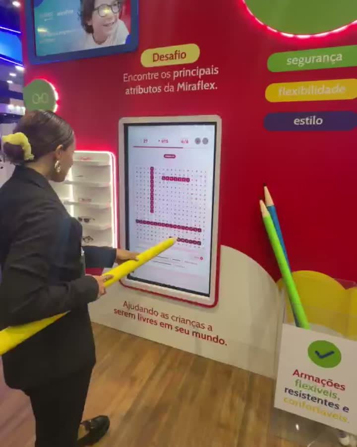 Participante jogando o caça-palavras na tela touch com um lápis cenográfico gigante