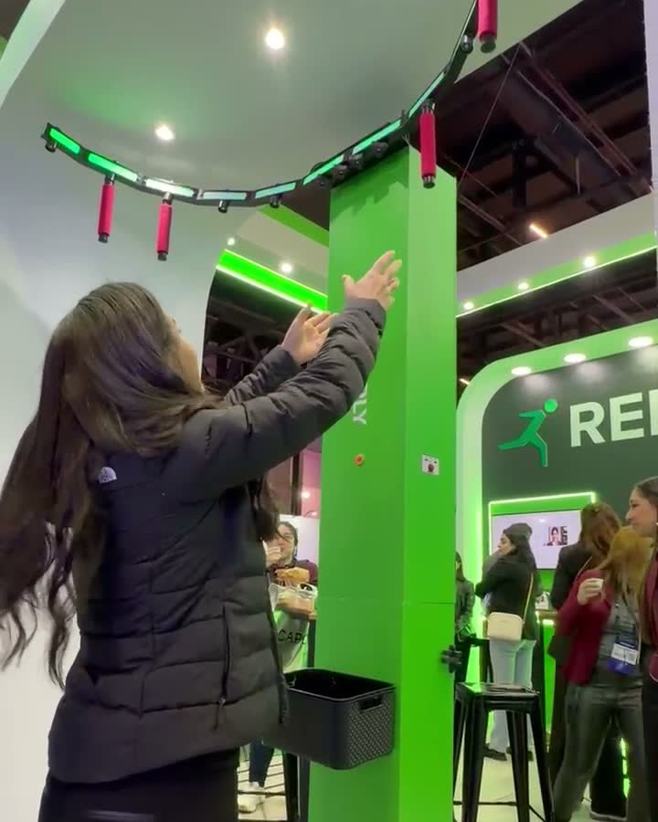 Participante de braços erguidos tentando pegar um bastão que solta do arco de LED