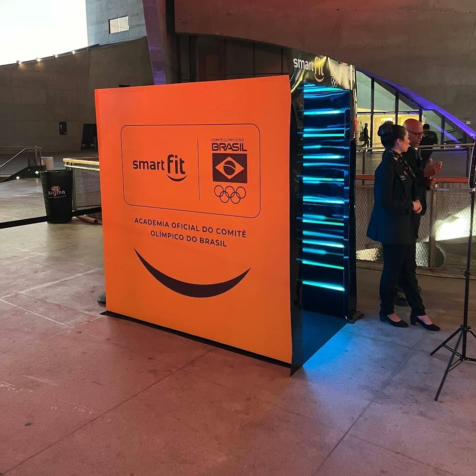 Lateral laranja do túnel com o logo da marca e o selo da parceria, e as fitas de LED azuis na abertura