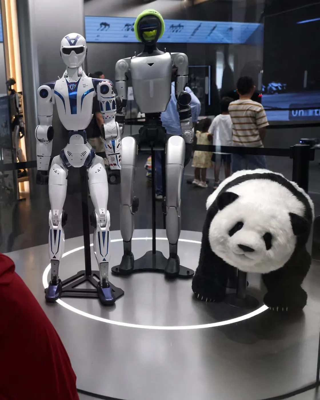 Humanoide R1, Humanoide G1 y Pooh Panda Robot lado a lado en una vitrina iluminada
